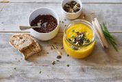 Glas mit gelber Suppe mit Brot und Körnern auf unbehandeltem Holztisch Glas mit gelber Suppe mit Brot und Körnern auf unbehandeltem Holztisch